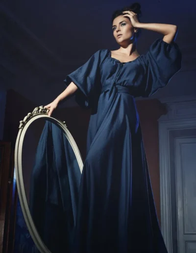 Elegant woman in a flowing navy kimono-sleeve gown posing with a vintage mirror, designed by Ibex Fashion Manufacturing for upscale U.S. fashion brands.