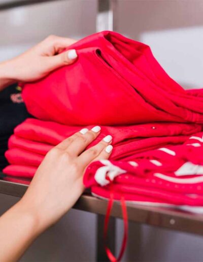 Close-up of a woman organizing folded red jeans on a retail shelf, representing private label clothing production and retail-ready apparel solutions.