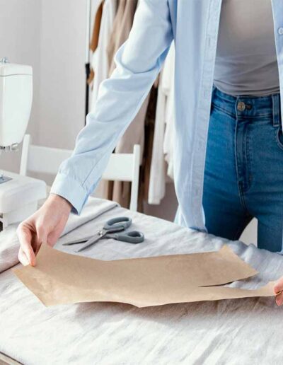 Fashion designer arranging paper pattern on fabric beside sewing machine, representing the garment development process at Ibex Fashion.