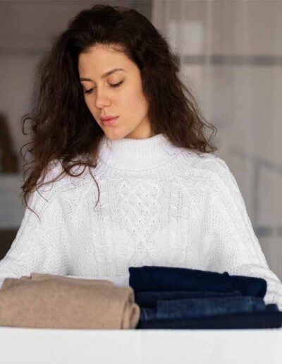 Young woman holding a box filled with folded sweaters and jeans, showcasing high-quality private label apparel ready for delivery.