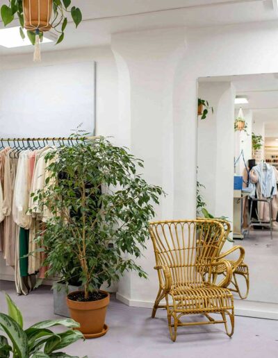 Modern sustainable clothing showroom with eco-friendly garments, natural plants, and rattan furniture at Ibex Fashion, a USA-based manufacturer offering worldwide shipping.